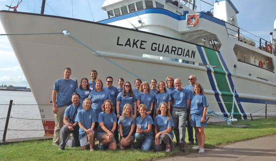 group of people pose in front of a large boat called the Research Vessel Lake Guardian