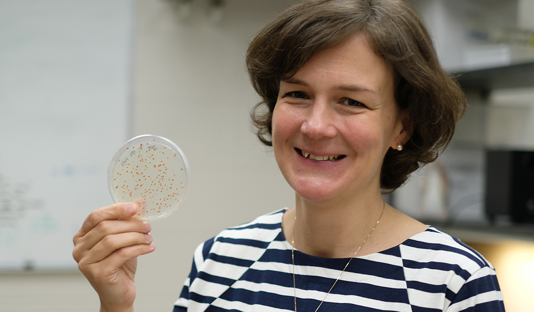 woman holds up a petri dish with visible microbes present