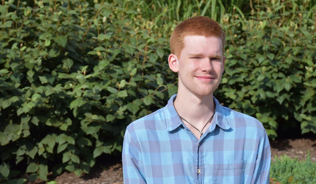 Jack Van Etten sits in front of green bushes