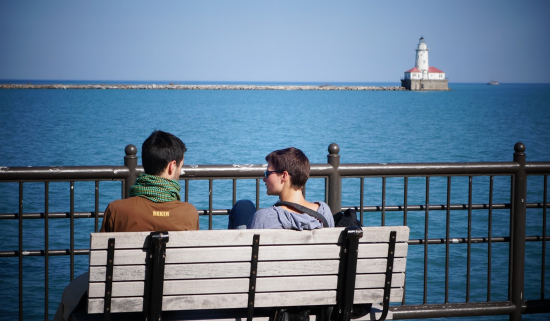 two young people sitting on a bench at the edge of Lake Michigan, with a lighthouse in the background