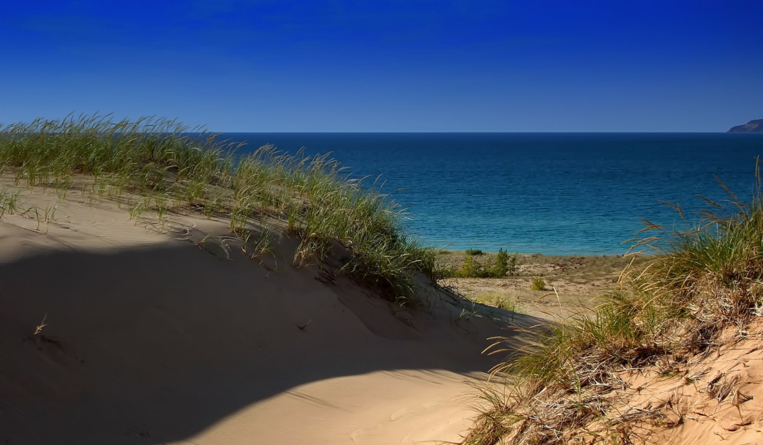 sand dunes and grass in the forefront, water of Lake Michigan in the background beyond the dunes