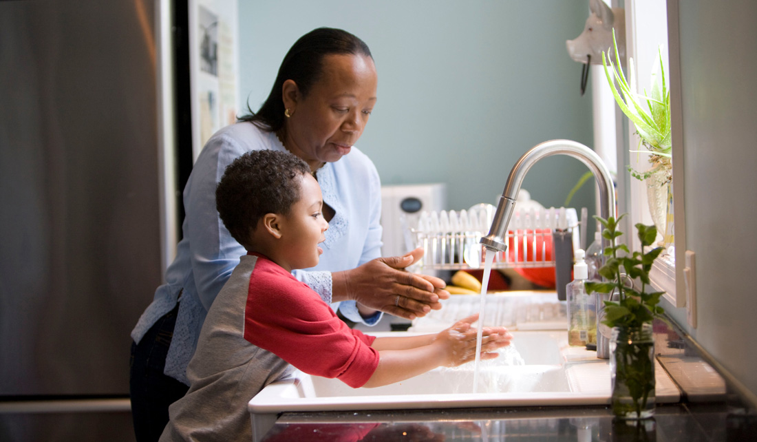 woman in long sleeve shirt standing beside boy in baseball tee washing hands