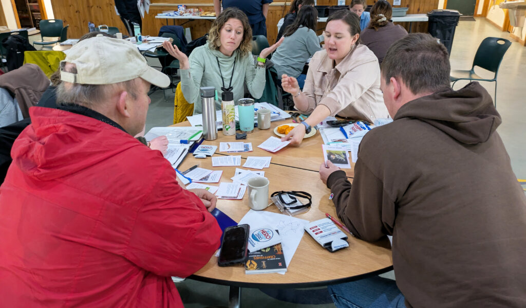 Four educators sitting at a round table are engaged in an activity from the crayfish curriculum