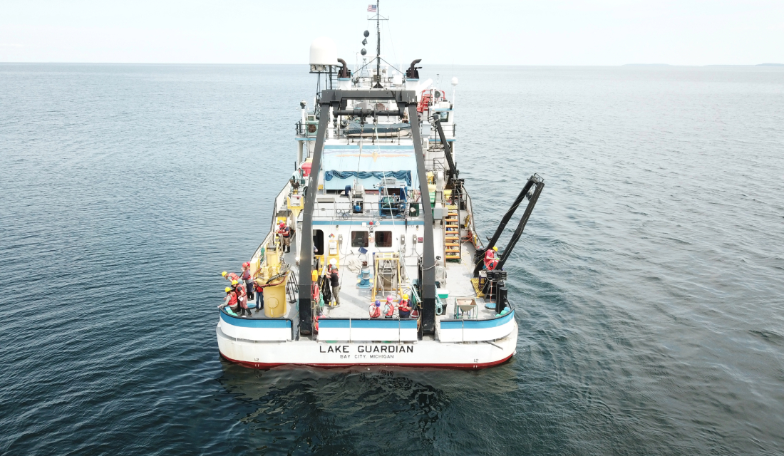 A large ship with crew working on board floats on lake water