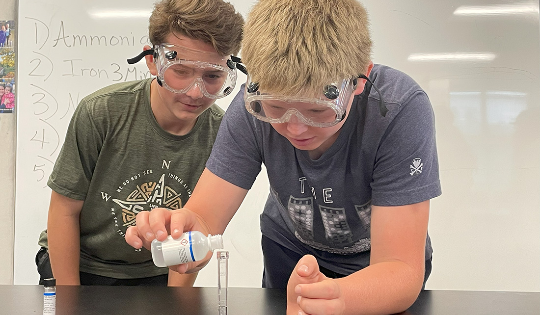 Two boys pouring liquid into a test tube