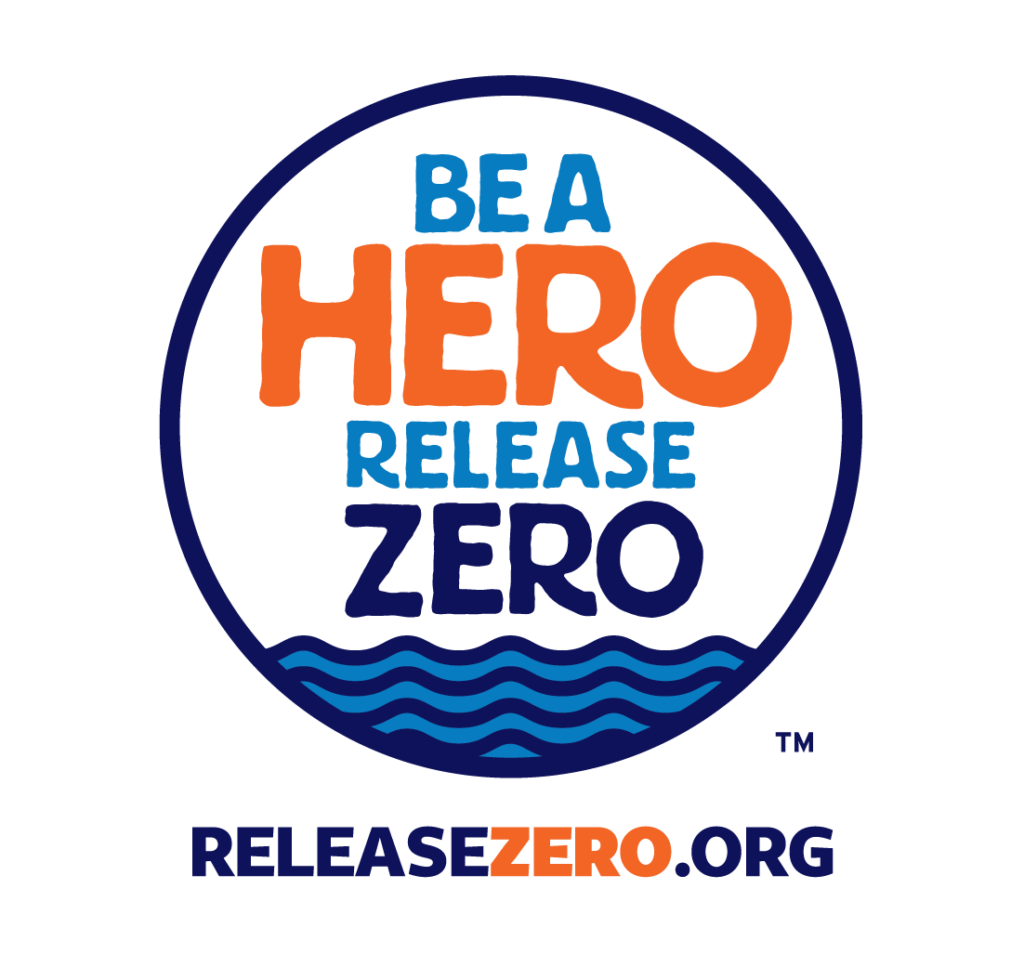 Circular “Be a Hero Release Zero” logo with blue and orange text inside a navy border. Stylized blue waves appear at the bottom of the circle, and “ReleaseZero.org” is written below.